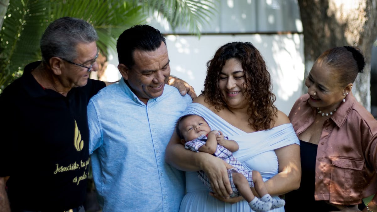 Joyful family gathering with proud parents and grandparents holding a newborn baby outdoors.